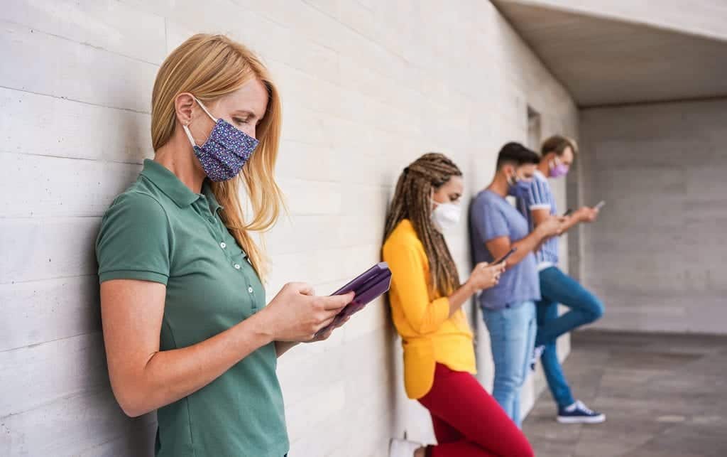Young people leaning against a wall while using their cellphones