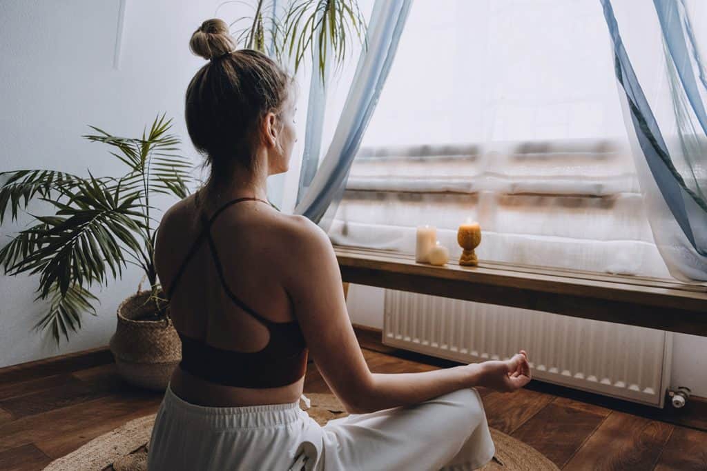 Woman doing yoga in front of her window Positive Quarantine Habits to Adopt