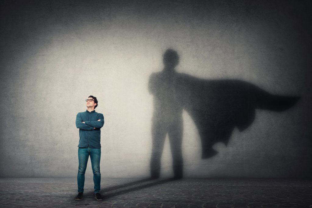 Brave man keeps arms crossed, looks confident, casting a superhero with cape shadow on the wall mental health for men