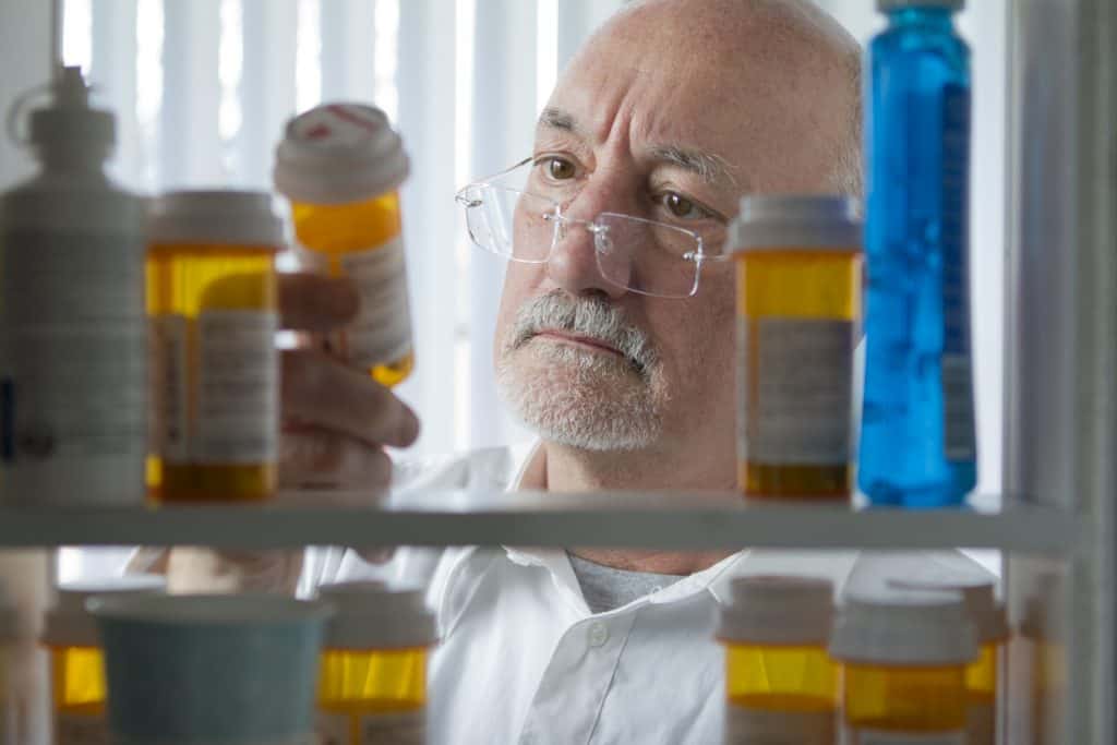 Older man looking at pill bottles in medicine cabinet