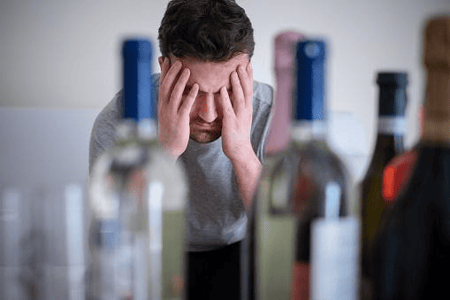 Man looking distressed behind multiple bottles of alcohol chemical dependency