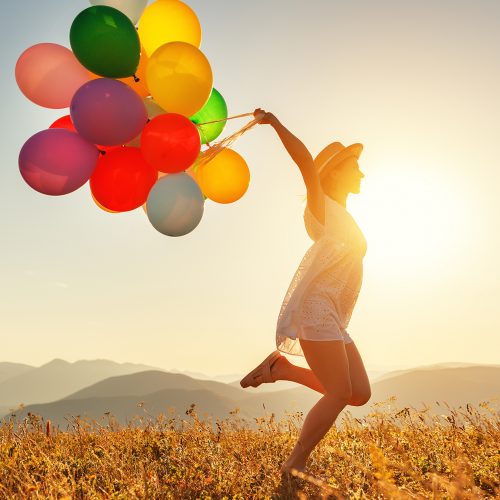 Woman running through a field with balloons